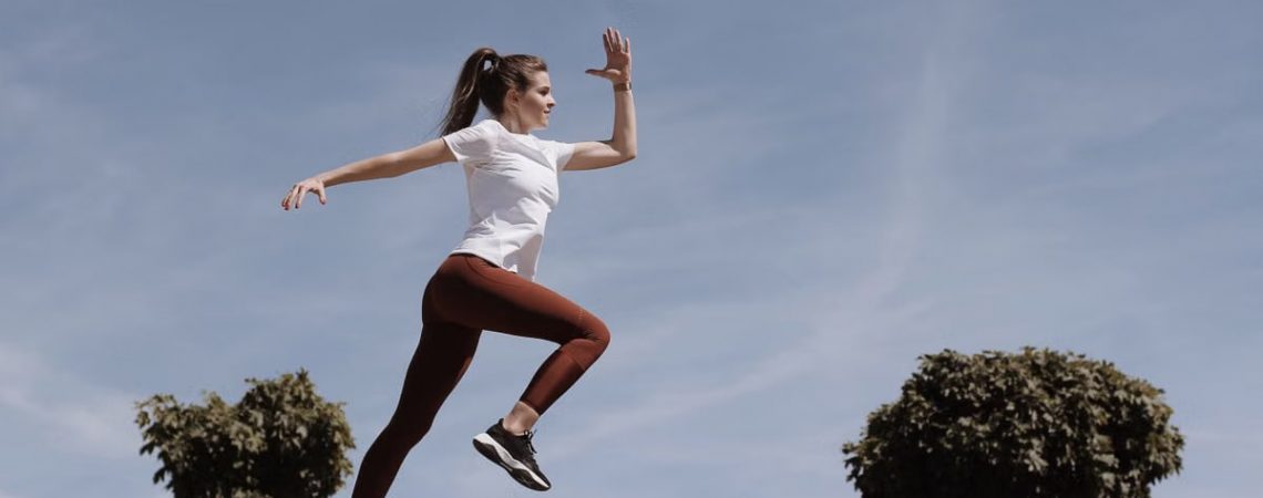 Athletic woman in action jump against a blue sky background. Captures fitness in motion.